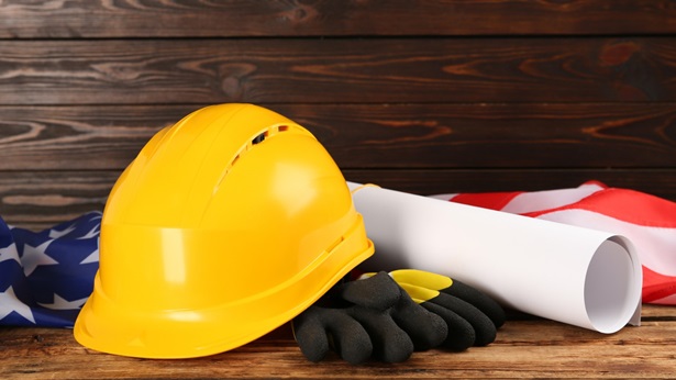 Hardhat and gloves next to an American flag and construction plans